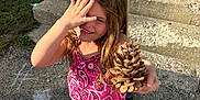 Phoenix is registered to the contest to win money with this photo: child, girl, pine_cone, pink_clothing, sneakers, outdoor, daylight, steps, house, concrete, gravel, smiling, playful, long_hair, hand, footwear, front_door, backpack, chalk, shadow
