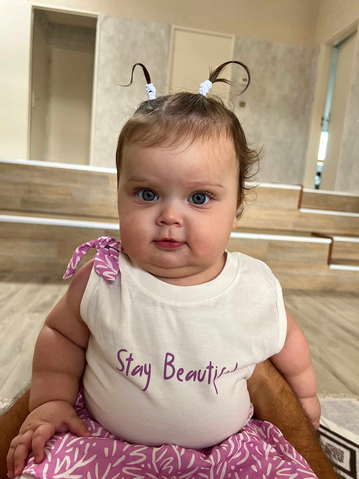 Mira participe au concours pour gagner de l'argent avec cette photo : baby, child, indoor, cute, pigtails, white_top, purple_clothing, chubby_cheeks, face, person, expression, sitting, floor, wooden_floor, steps, arms, hand, looking_at_camera, casual_clothing, portrait