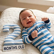 Rylee joined the competition — help win amazing prizes! baby, infant, smiling, striped_clothing, plush_number, number_two, months_old_sign, blanket, cozy, indoors, happy, cute, portrait, child, newborn, lying_down, celebration, milestone, soft_toys, window_light