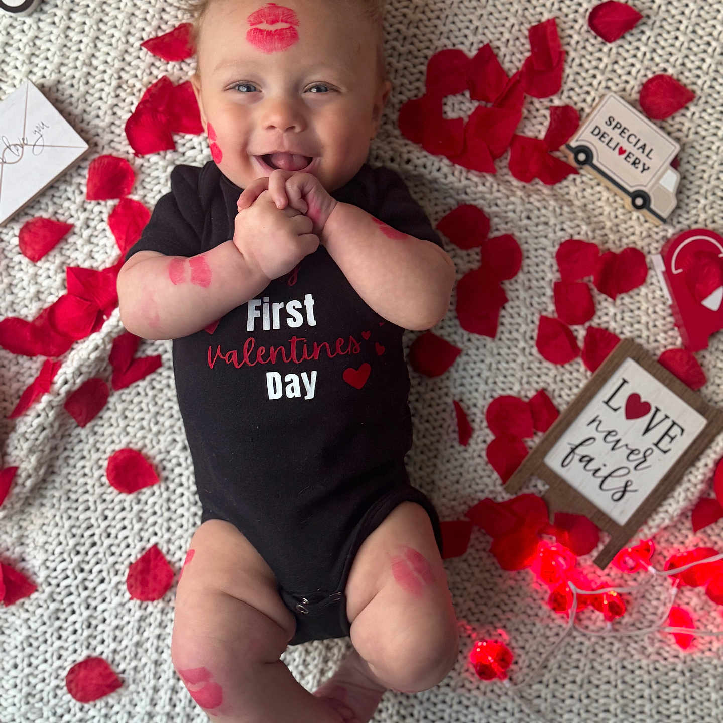 Kris joined the competition — help win amazing prizes! baby, black_onesie, blanket, cute, decorations, face, hands, happy, heart, infant, kiss_marks, knit_texture, legs, love_theme, portrait, red_rose_petals, sign, smiling, special_delivery, valentines_day
