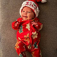 Emery is registered to the contest to win money with this photo: baby, infant, smiling, christmas_hat, red_pajamas, gingerbread_man, christmas_tree, holiday, festive, cute, lying_down, cozy, soft_texture, happy, child, portrait, indoors, celebration, seasonal, warm_clothing