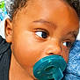 baby, pacifier, close_up, child, curly_hair, blue_pacifier, infant, face, portrait, lying_down, blanket, soft_texture, cute, young_child, black_clothing, skin, eyelashes, expression, indoors, resting