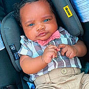 Amor is registered to the contest to win money with this photo: baby, child, car_seat, bowtie, shirt, pants, seatbelt, safety_label, cute, portrait, infant, clothing, hands, face, blue_eyes, hair, cushion, seat, indoor, young
