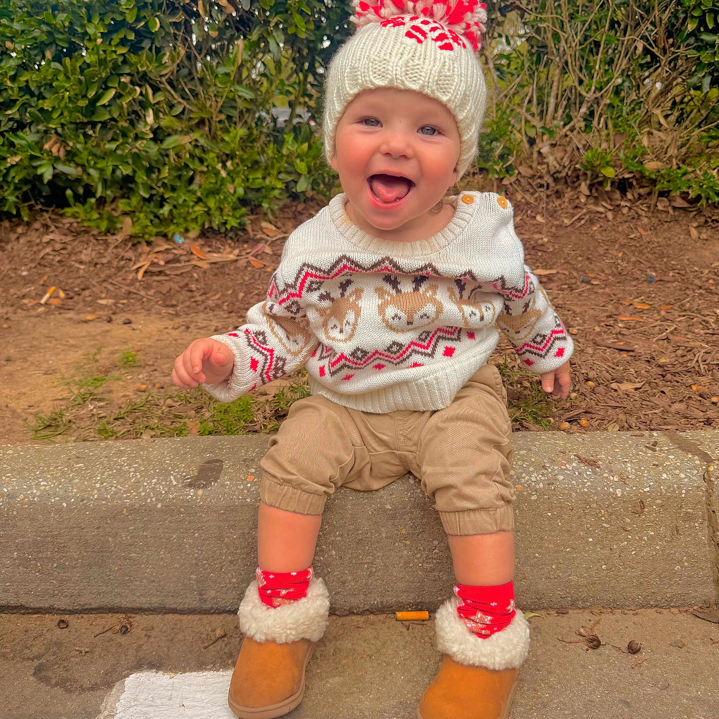 Kohen-Lee is registered to the contest to win money with this photo: beige, boots, child, clothing, curb, cute, fall, greenery, happy, hat, nature, outdoor, pants, person, pom_pom, red, seasonal, smiling, sweater, toddler