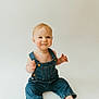 baby, child, denim_overalls, smiling, sitting, barefoot, light_background, cute, happy, portrait, infant, young_child, studio_photo, casual_clothing, one_person, small_child, indoors, face, skin, blond_hair