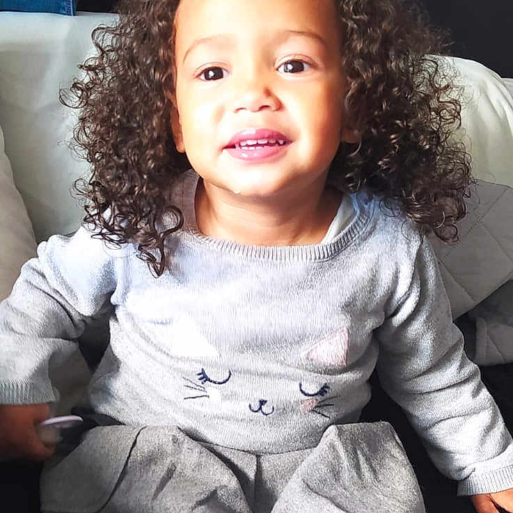 Kimberly participe au concours pour gagner de l'argent avec cette photo : black_tights, casual, cat_design, child, clothing, couch, curly_hair, cute, furniture, grey_dress, happy, home, indoor, long_sleeves, person, portrait, sitting, smiling, toddler, young