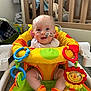Jude is registered to the contest to win money with this photo: baby, child, infant, sitting, toy, activity_center, feeding_tube, medical_tape, colorful, orange_socks, crib, stuffed_animal, nursery, happy, smiling, indoor, floor, playtime, cute, person
