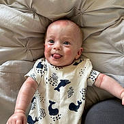 Jude is registered to the contest to win money with this photo: baby, child, infant, onesie, whale_print, cushion, beige, tufted, tongue_out, happy, smile, face, arm, skin, lying_down, clothing, indoors, cute, expression, person