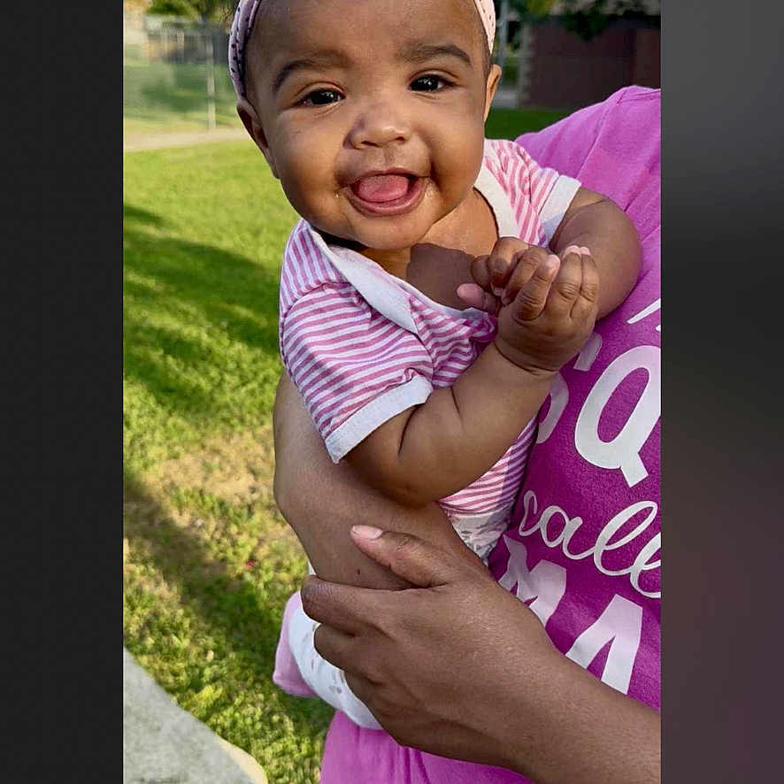 Veronica-Faith is registered to the contest to win money with this photo: adult_hand, baby, casual_clothing, child, closeup, cute, daylight, grass, greenery, happy, headband, holding, infant, nature, outdoor, person, pink, portrait, smiling, striped_shirt