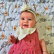 Jasmine is registered to the contest to win money with this photo: baby, child, smiling, headband, flower, red_dress, checkered_pattern, blanket, animal_print, lying_down, happy, cute, portrait, infant, indoors, clothing, face, hand, young_child, adorable