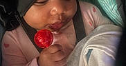 Honesty is registered to the contest to win money with this photo: baby, child, lollipop, blanket, hat, black_bonnet, pink_clothing, hand, face, infant, cute, indoor, cozy, person, holding, sweet, young_child, closeup, seat, curious