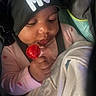 baby, child, lollipop, blanket, hat, black_bonnet, pink_clothing, hand, face, infant, cute, indoor, cozy, person, holding, sweet, young_child, closeup, seat, curious