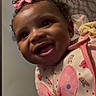 baby, child, infant, smiling, happy, portrait, close_up, curly_hair, hair_bow, pink_outfit, butterfly_pattern, indoor, home, bedroom, fabric, blanket, patterned_background, sitting, joyful, photograph