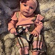 Peyton is registered to the contest to win money with this photo: baby, infant, newborn, headband, bow, pink_clothing, plaid_overalls, blanket, furry_blanket, portrait, blue_eyes, hands, feet, toes, cozy, soft_texture, adorable, indoor, nursery_fashion, sitting