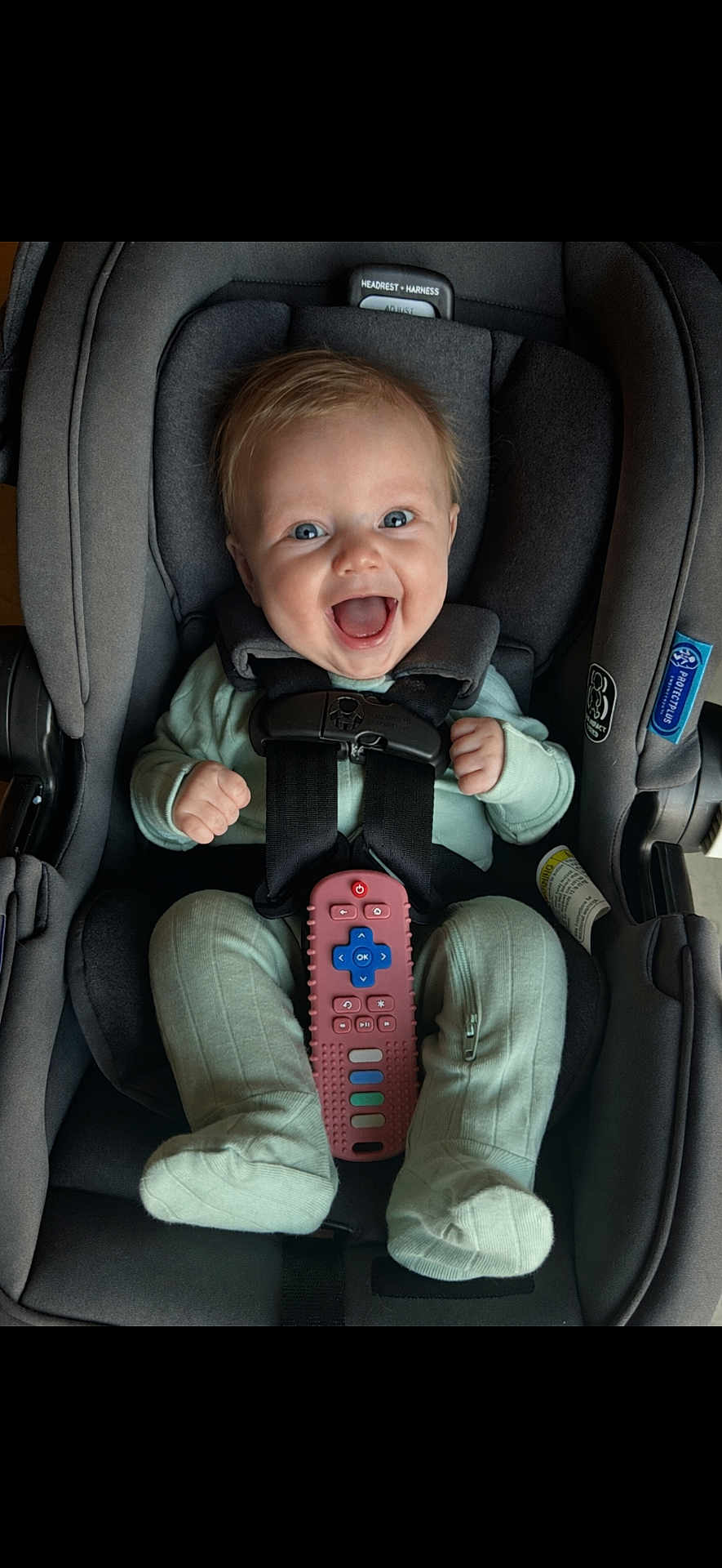 Peyton joined the competition — help win amazing prizes! baby, infant, child, smiling, happy, car_seat, harness, seat_belt, remote_control, toy, onesie, green_clothing, socks, blue_eyes, headrest, buckle, portrait, closeup, indoor, joyful