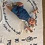 baby, child, infant, denim_overalls, stuffed_animal, toy, milestone_blanket, numbers, text, floor, carpet, smiling, cute, lying_down, happy, clothing, footwear, sock, indoor, portrait