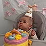 baby, birthday_cake, high_chair, party_hat, pink_bows, frosting, rainbow_cake, celebration, child, cake, pastel_colors, cute, happy, indoor, food, dessert, face, smile, person, event