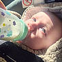baby, infant, bottle, car_seat, seat_belt, feeding, blue_eyes, close_up, sunlight, blanket, coat, hand, warning_label, upholstery, milk, hooded_jacket, face, portrait, eyes, newborn
