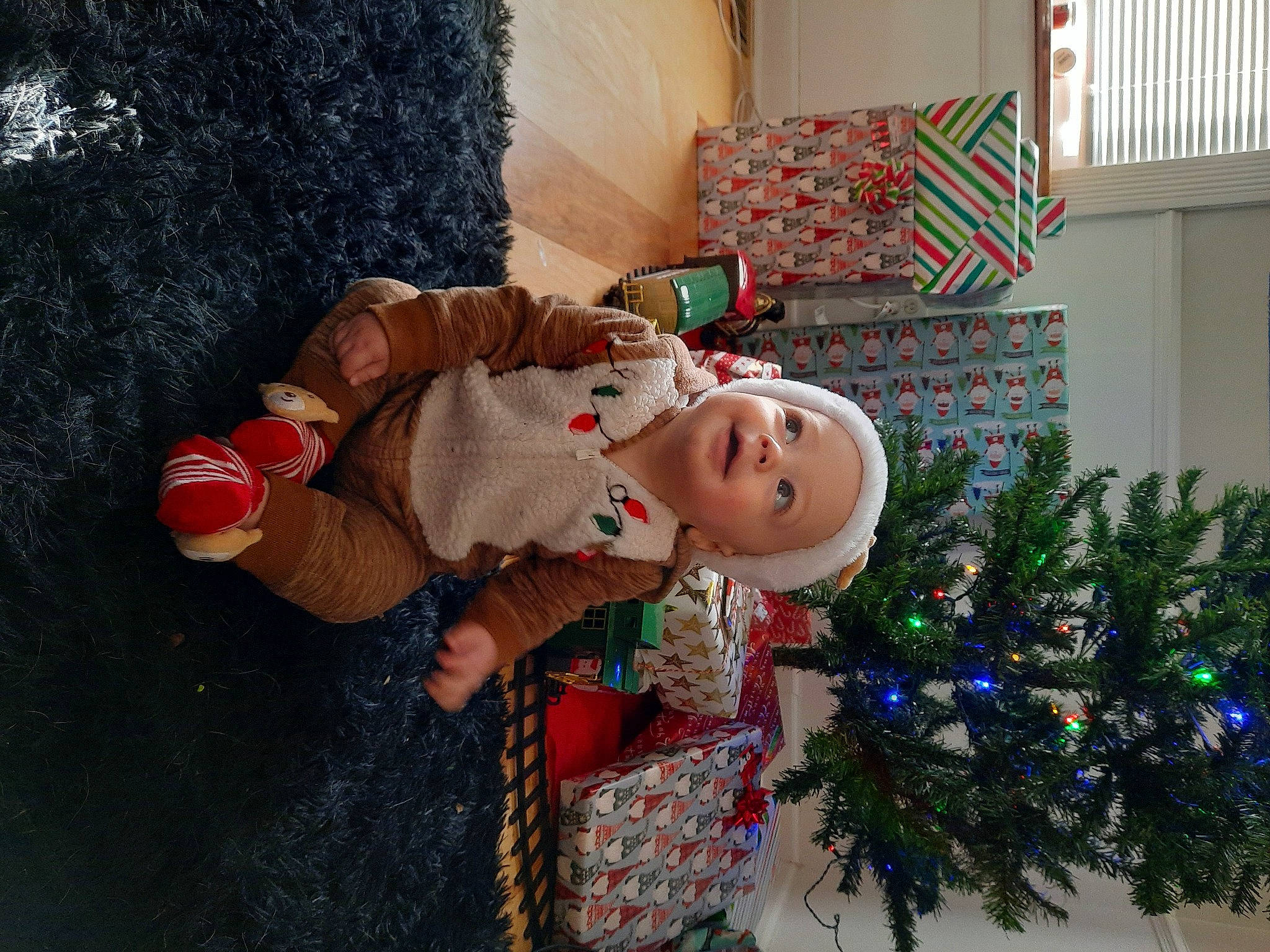 Desmond is registered to the contest to win money with this photo: baby_toddler_clothing, christmas, christmas_decoration, christmas_eve, christmas_ornament, christmas_tree, conifer, event, evergreen, fun, holiday, holiday_ornament, living_room, ornament, room, toddler, toy, tree, winter, wood