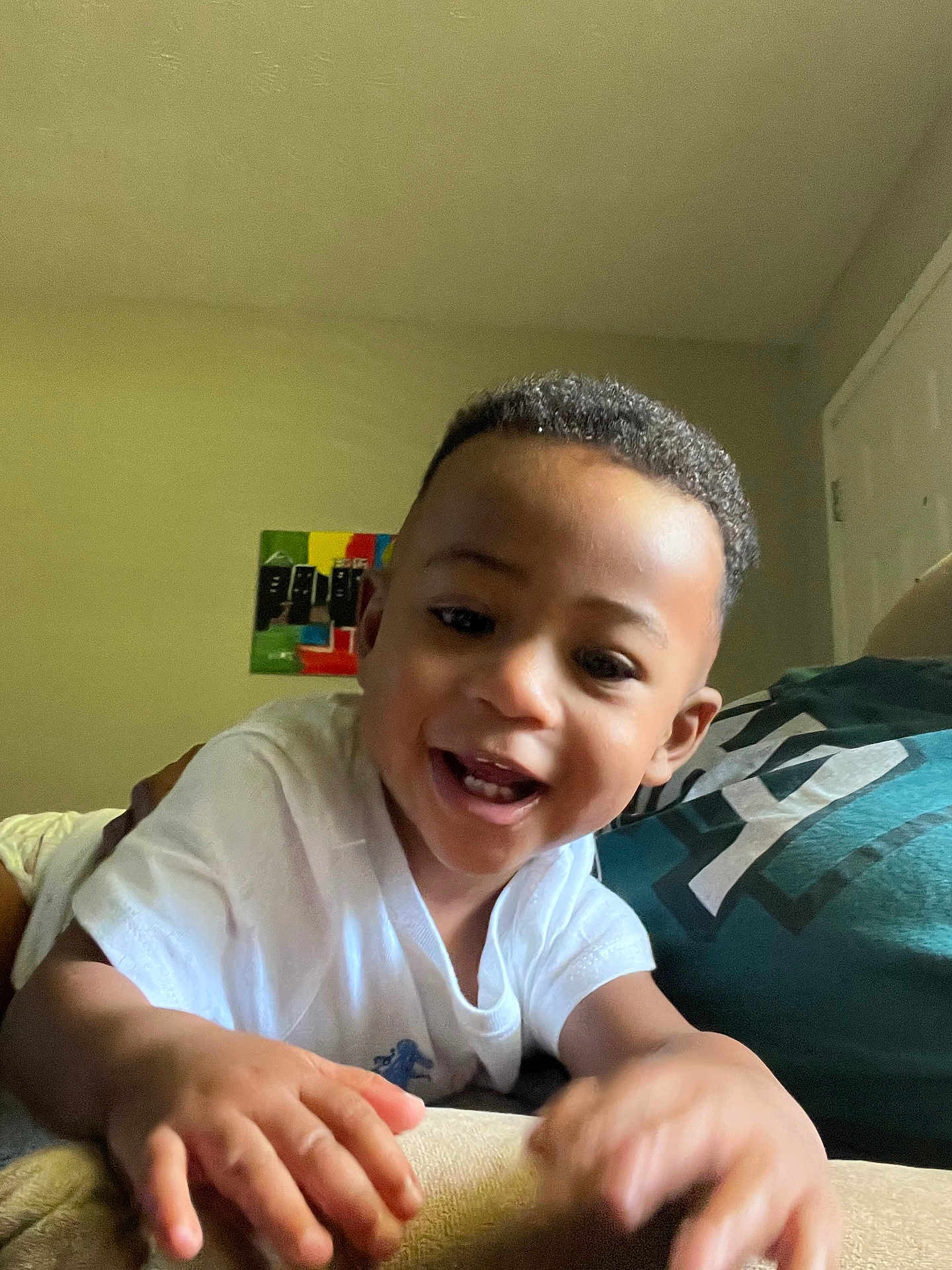 Tristen joined the competition — help win amazing prizes! toddler, child, smiling, indoor, white_shirt, curly_hair, person, hand, face, happy, couch, pillow, wall_art, colorful, playful, young_child, portrait, expression, human, casual