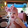 baby, child, pink_bow, headband, floral_outfit, restaurant, booth, table, glass, straw, window, greenery, poster, sports, hands, smile, happy, indoor, person, infant