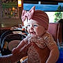 Scarlett is registered to the contest to win money with this photo: baby, child, smiling, headband, pink_bow, floral_pajamas, hands, restaurant, table, drink, blue_drink, car_seat, adult, watch, bracelet, window, photograph, sports_photo, indoor, happy