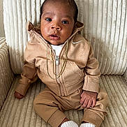 Tayden is registered to the contest to win money with this photo: baby, infant, child, tracksuit, hoodie, gold_chain, white_socks, armchair, texture, beige, tan, cute, portrait, sitting, indoor, person, fashion, young, cozy, clothing