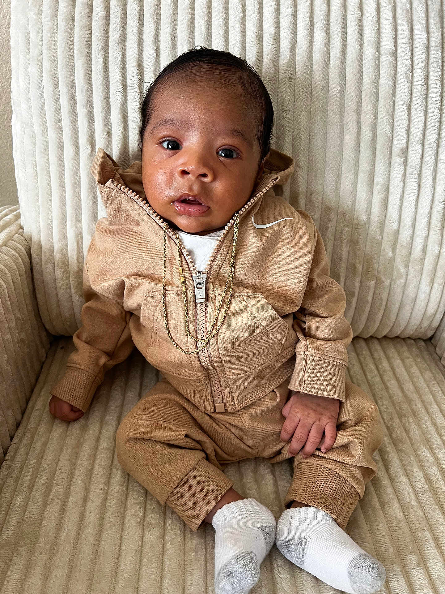 Tayden is registered to the contest to win money with this photo: baby, infant, child, tracksuit, hoodie, gold_chain, white_socks, armchair, texture, beige, tan, cute, portrait, sitting, indoor, person, fashion, young, cozy, clothing