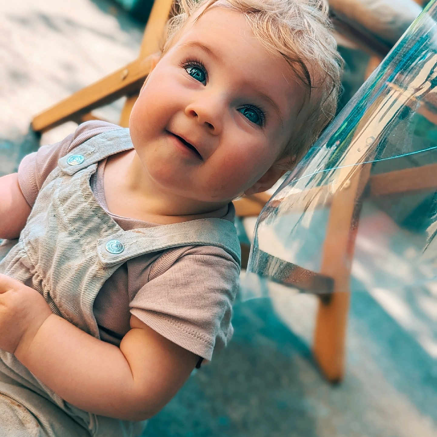 Izya a rejoint le concours — aidez-le/la à gagner de superbes lots ! baby, blonde_hair, blue_eyes, candid, casual_clothing, child, close_up, curious, face, floor, happy, natural_light, outdoor, overalls, person, portrait, short_sleeves, smiling, toddler, wooden_chair