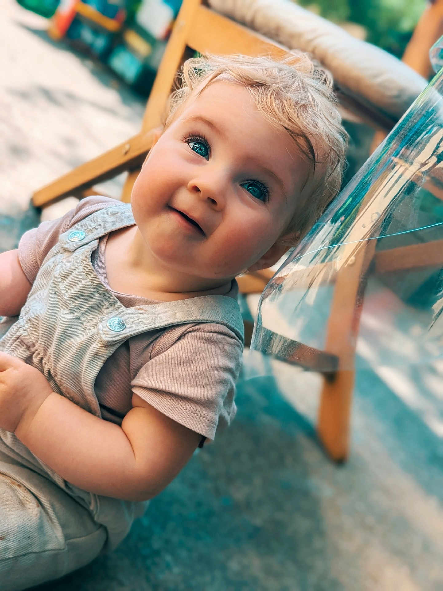 Izya a rejoint le concours — aidez-le/la à gagner de superbes lots ! baby, blonde_hair, blue_eyes, candid, casual_clothing, child, close_up, curious, face, floor, happy, natural_light, outdoor, overalls, person, portrait, short_sleeves, smiling, toddler, wooden_chair