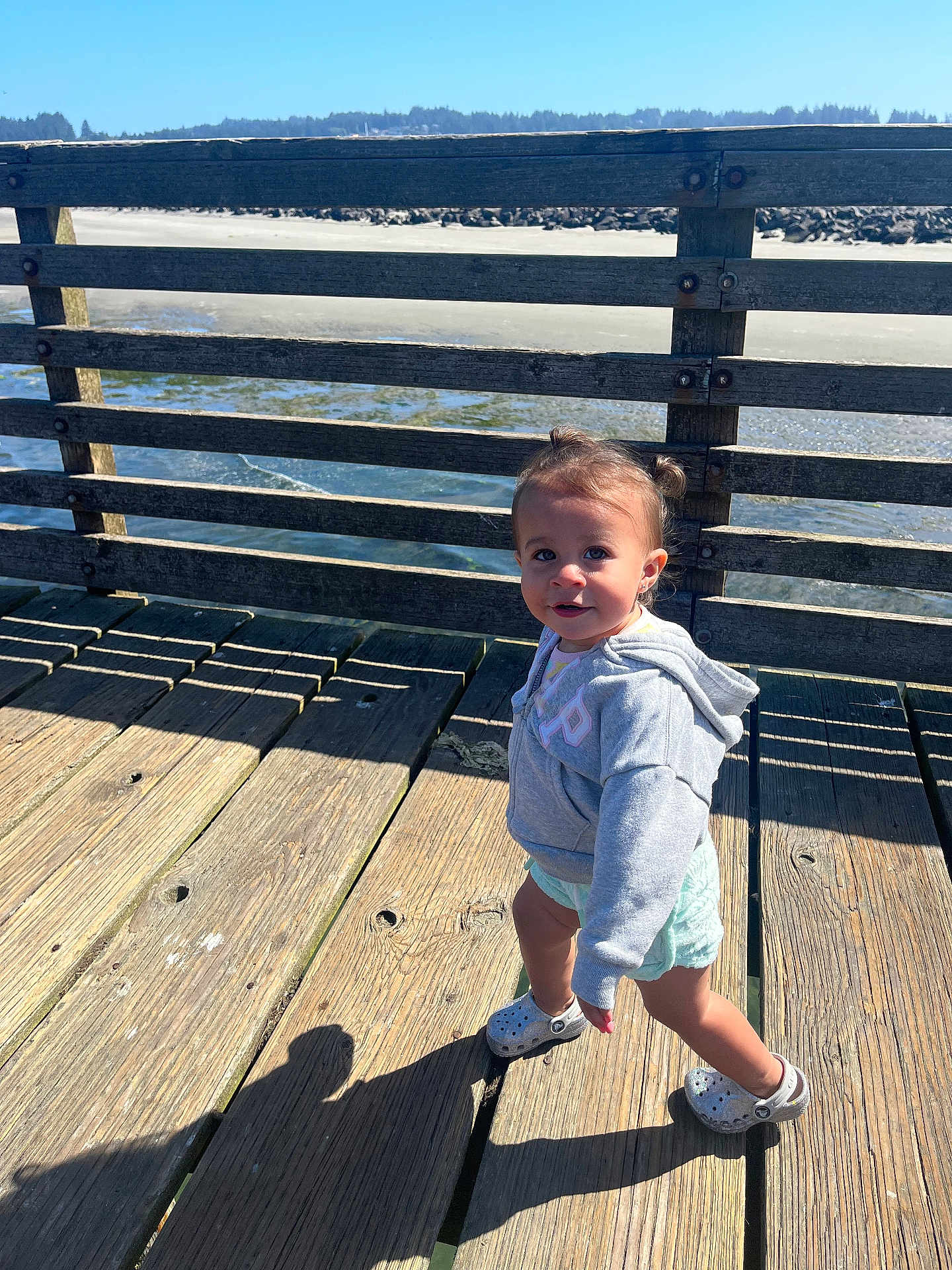 Bayley is registered to the contest to win money with this photo: toddler, child, pier, wooden_planks, water, outdoor, sunlight, shadow, hoodie, shorts, footwear, pigtails, person, nature, sky, summer, daytime, cute, walking, casual