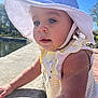 Bayley is registered to the contest to win money with this photo: toddler, child, hat, sunhat, yellow_striped_clothing, outdoor, daylight, water, stone_ledge, blue_sky, nature, trees, portrait, closeup, cute, baby, person, sunlight, summer, curious