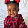 toddler, child, girl, red_bows, pigtails, plaid_dress, bed, white_bedspread, indoor, portrait, smiling, cute, young_child, curly_hair, red_clothing, holding_object, happy, person, baby, comfort
