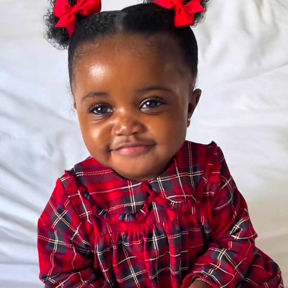 Khardiatou participe au concours pour gagner de l'argent avec cette photo : toddler, child, girl, red_bows, pigtails, plaid_dress, bed, white_bedspread, indoor, portrait, smiling, cute, young_child, curly_hair, red_clothing, holding_object, happy, person, baby, comfort