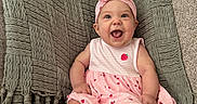 Riley is registered to the contest to win money with this photo: baby, infant, child, smiling, happy, portrait, sitting, indoors, couch, blanket, pink_dress, headband, bow, strawberry_pattern, textile, furniture, home, closeup, barefoot, photography