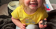 Sawyer is registered to the contest to win money with this photo: background, barefoot, blanket, child, cookie, cozy, face, fan, furniture, hair, happy, indoor, leggings, person, room, sitting, smiling, toddler, toy, yellow_shirt
