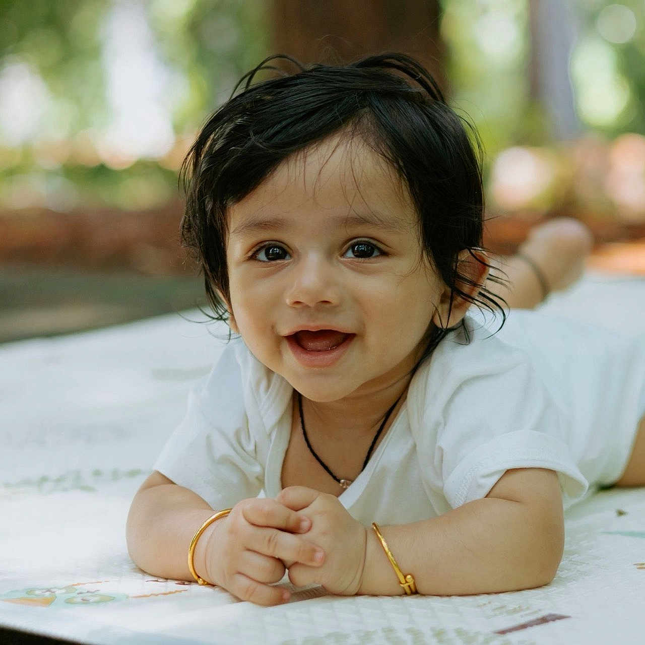 Aabir joined the competition — help win amazing prizes! baby, background_blur, black_hair, bracelet, child, cute, daylight, expression, face, hands, happy, lying_down, mat, nature, outdoor, portrait, skin, smiling, toddler, white_clothing