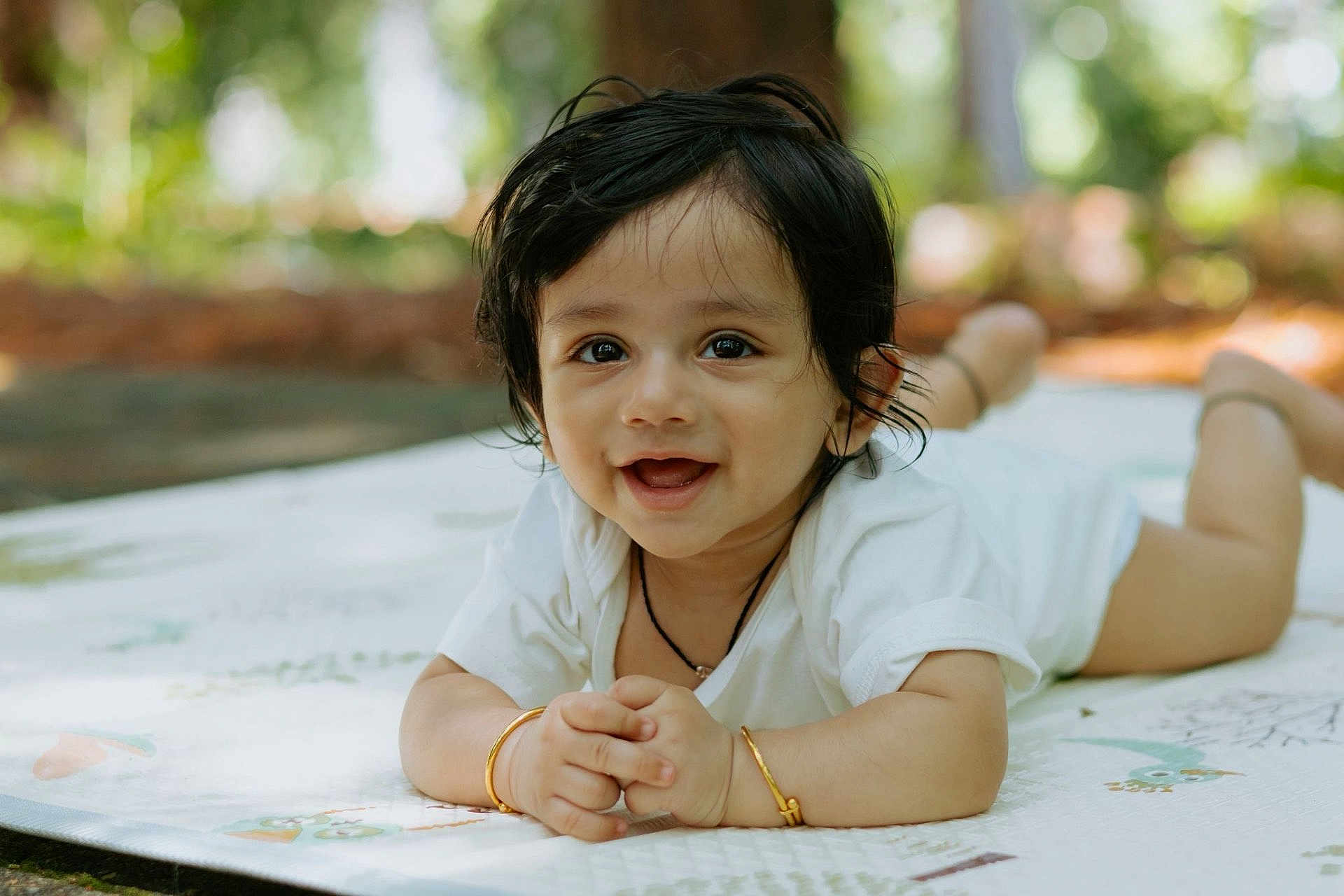 Aabir joined the competition — help win amazing prizes! baby, background_blur, black_hair, bracelet, child, cute, daylight, expression, face, hands, happy, lying_down, mat, nature, outdoor, portrait, skin, smiling, toddler, white_clothing