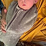 Oakley joined the competition — help win amazing prizes! baby, infant, child, swaddled, blanket, yellow_blanket, gray_clothing, portrait, close_up, face, eyes, wide_eyed, indoor, cozy, sleeping_area, adult_hand, supported, cuddled, soft_fabric, photography