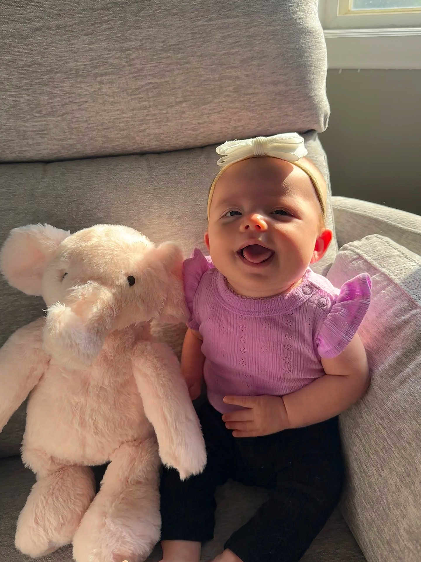 Maycie joined the competition — help win amazing prizes! baby, child, plush_toy, elephant, pink, purple, headband, smiling, happy, couch, indoor, sunlight, window, furniture, soft_toy, infant, clothing, cute, seated, portrait