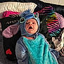 baby, costume, blue, pillow, blanket, couch, indoor, child, cute, plush, face, person, clothing, soft, seated, young, expression, colorful, fabric, headwear