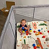 baby, child, infant, smiling, laughing, sitting, playpen, play_mat, colorful_balls, toy, blue_ball, indoor, nursery, floor, cardboard_box, home, portrait, happy, playtime, animal_pattern