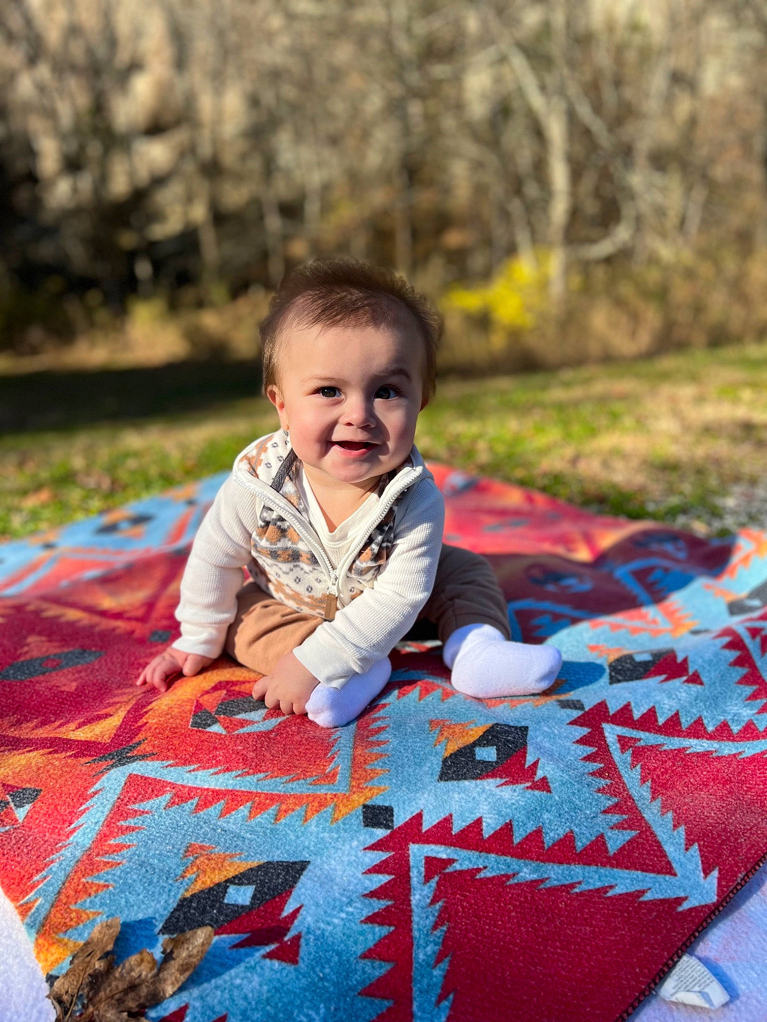 Forrest is registered to the contest to win money with this photo: baby, child, flooring, fun, grass, happy, jacket, joy, leisure, linens, pattern, people_in_nature, person, plant, play, recreation, sitting, smile, toddler, tree