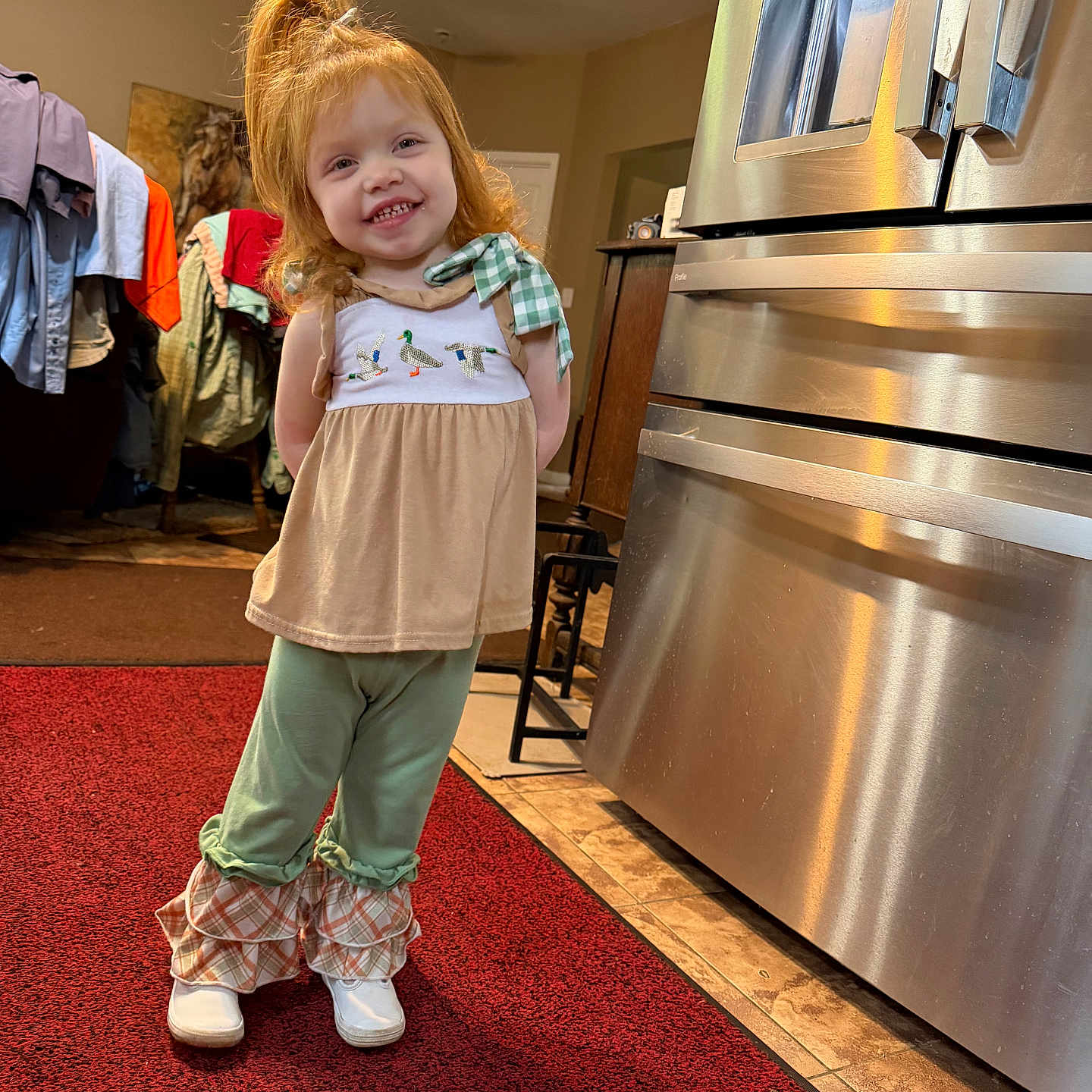 Lainey is registered to the contest to win money with this photo: child, girl, red_hair, smiling, standing, indoor, kitchen, refrigerator, carpet, clothing, white_shoes, ruffled_pants, ceiling_fan, door, furniture, home, light, portrait, happy, person