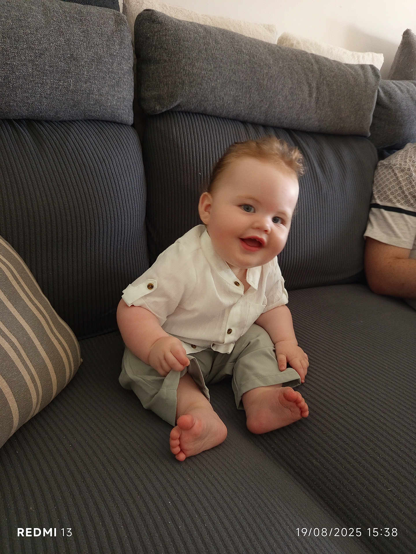 Gabriel a rejoint le concours — aidez-le/la à gagner de superbes lots ! baby, smiling, sitting, couch, gray_couch, pillow, striped_pillow, white_shirt, khaki_pants, barefoot, feet, chubby_cheeks, happy, indoor, portrait, candid, timestamp, watermark, person, home