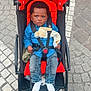 baby, stroller, red, blue_shirt, denim_jeans, soft_toy, pacifier, cobblestone, outdoor, child, serious_face, footwear, socks, baby_clothing, seatbelt, toy_bunny, sidewalk, urban, street, infant
