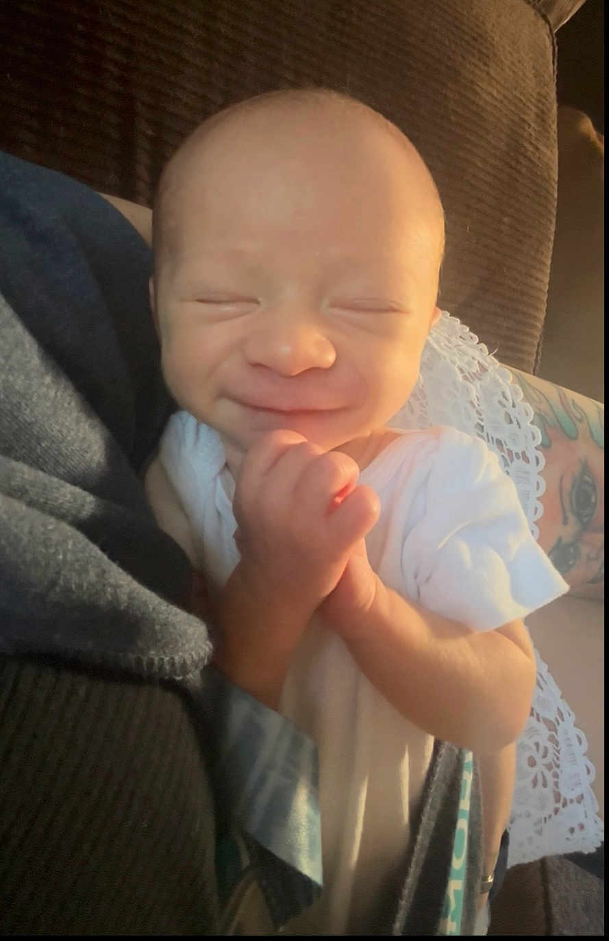 Levi is registered to the contest to win money with this photo: baby, smiling, infant, hands, clasped_hands, white_clothing, tattoo, arm, lace, fabric, soft_lighting, close_up, indoor, person, newborn, cute, peaceful, portrait, skin, face