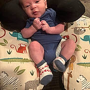 Levi is registered to the contest to win money with this photo: baby, infant, blue_onesie, socks, animal_print, cushion, neck_pillow, indoor, cute, child, person, resting, comfort, soft_furniture, face, head, legs, hands, expression, newborn