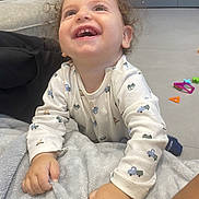 Arié a rejoint le concours — aidez-le/la à gagner de superbes lots ! toddler, child, curly_hair, smiling, blanket, indoor, living_room, toys, furniture, happy, clothing, person, couch, floor, hand, face, expression, home, playful, casual