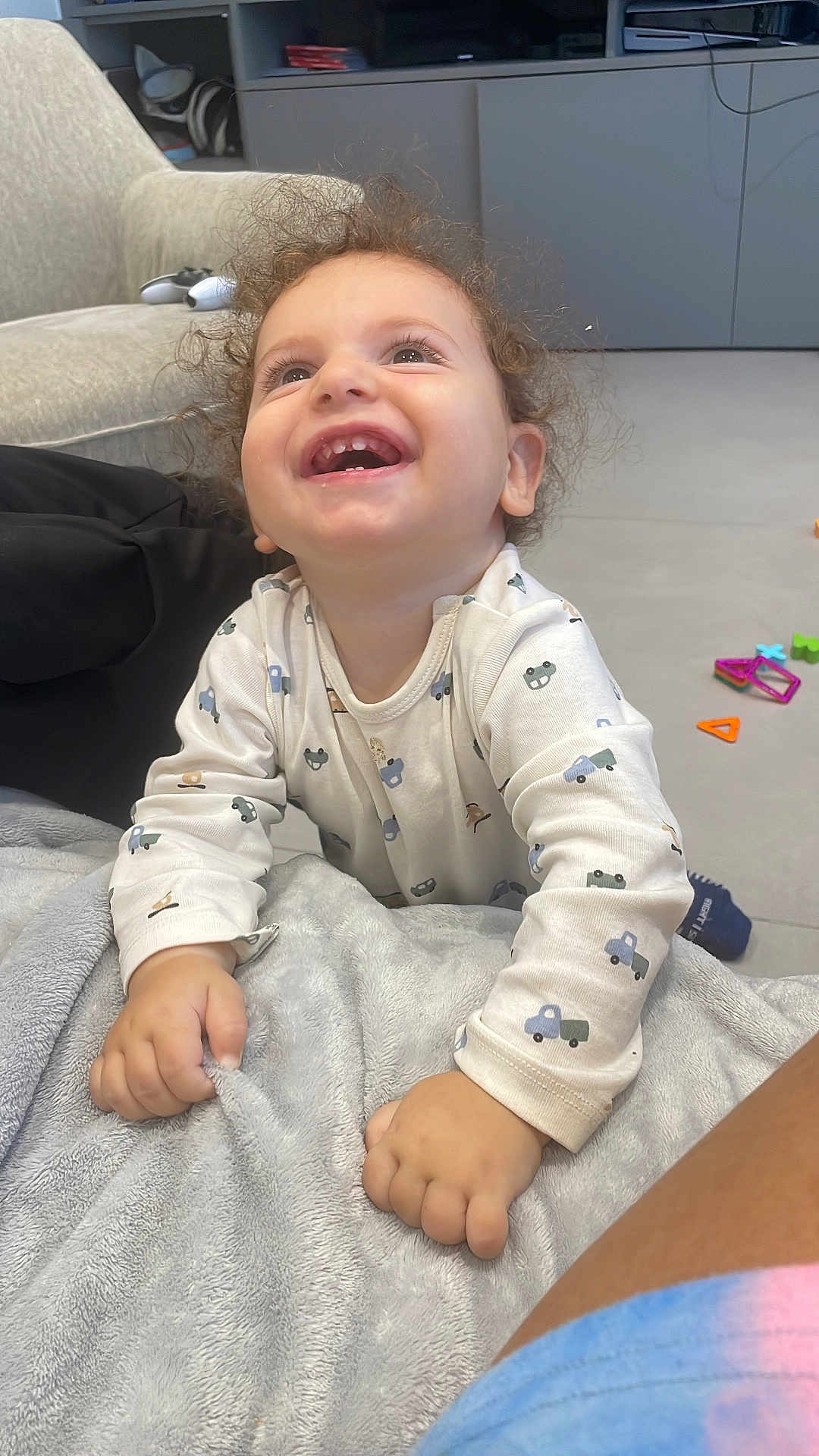 Arié a rejoint le concours — aidez-le/la à gagner de superbes lots ! toddler, child, curly_hair, smiling, blanket, indoor, living_room, toys, furniture, happy, clothing, person, couch, floor, hand, face, expression, home, playful, casual